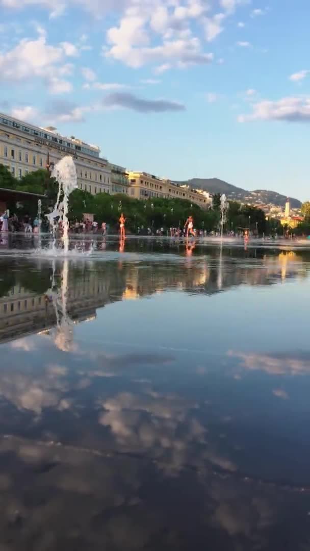Francja, Nicea, 04 sierpnia 2018: Pionowe nagranie tego dziecka igrającego w fontannie w centrum Nicei w ciepły słoneczny wieczór, lustrzany obraz nieba w kałużach fontanny — Wideo stockowe