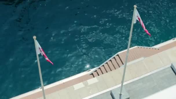 モナコ,モンテカルロ, 08 7月2019:晴れた日に風の中でモナコの新しいヨットクラブの旗,水は背景に紺碧です,ヘラクレスの港の遊歩道 — ストック動画