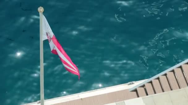 Monaco, Monte-Carlo, 08 luglio 2019: La bandiera del nuovo yacht club di Monaco nel vento nel tempo soleggiato, l'acqua è azzurra sullo sfondo, il lungomare del porto di Ercole — Video Stock