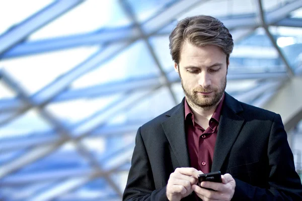 Homme d'affaires de quarante ans debout à l'intérieur d'un immeuble de bureaux moderne à la recherche d'un téléphone mobile — Photo