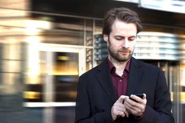 40-jähriger Geschäftsmann steht vor modernem Bürogebäude und schaut auf sein Handy — Stockfoto