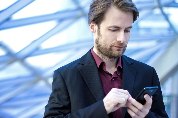 40-jähriger Geschäftsmann steht in modernem Bürogebäude und schaut auf sein Handy — Stockfoto