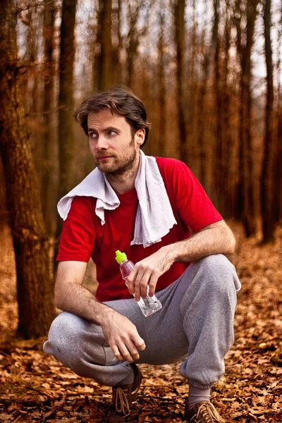 40 歳ランナー男水を飲むと秋の森でトレーニングをジョギングした後の残りを有する — ストック写真