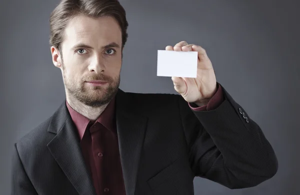 Veertig jaar oude ernstige zakenman presenteren blanco visitekaartje op een grijze achtergrond. de invoering van bedrijf concept. — Stockfoto