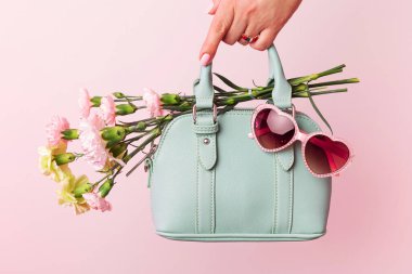 Kadınlar için moda bahar aksesuarları. Küçük nane yeşili el çantası (çanta), kalp şeklinde güneş gözlüğü ve pastel pembe arka planda çiçekler. Boş kopya (metin) alanı.