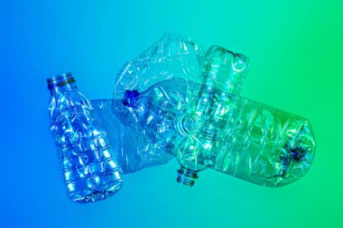 Geri dönüşüm ve ekoloji - ezilmiş, şeffaf, parlak mavi ve yeşil arka planda plastik şişeler.