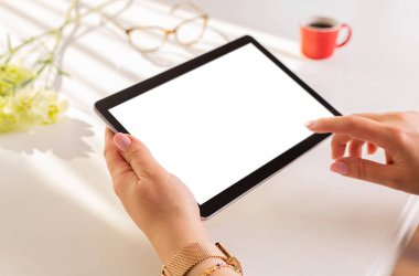 Kadının elleri tableti boş bir ekranla kapatıyordu. Arka plan olarak bahar çiçekleri, kahve ve beyaz masa. Boş kopya (metin) alanı.