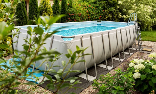 Long, above ground, rectangular, rack (frame) swimming pool outdoor in the garden. Summer holiday (vacation) and recreation.
