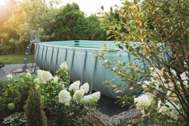 Long, above ground, rectangular, rack (frame) swimming pool outdoor in the beautiful garden nook. Summer holiday (vacation) and recreation.