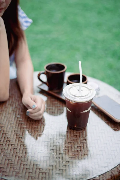 Iced black coffee on the table with a woman's hand placed, close up