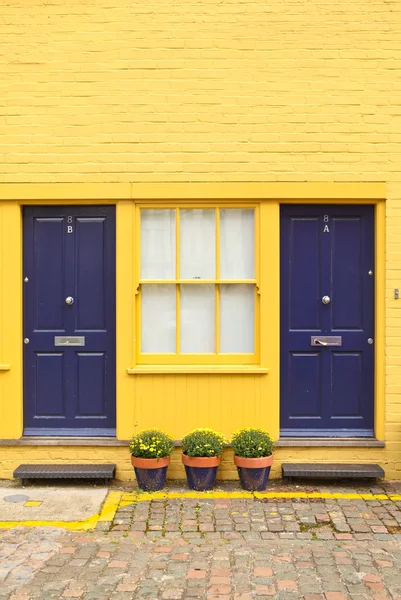 sundurma ile koyu mavi kapı, sarı tuğla ve beyaz windows.