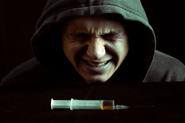 Grunge beeld van een depressief drugsverslaafde kijken naar een spuit en drugs — Stockfoto