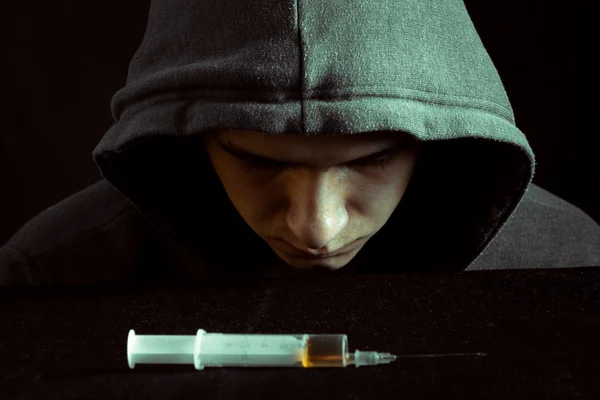 Grunge bilde av en deprimert narkoman som ser på en sprøyte og narkotika – stockfoto