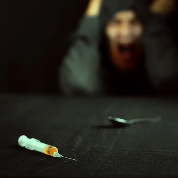 Grunge image of a depressed drug addict looking at a syringe and drugs — Stock Photo, Image