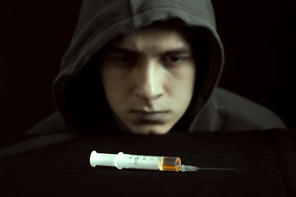 Grunge image of a depressed drug addict looking at a syringe and drugs — Stock Photo, Image