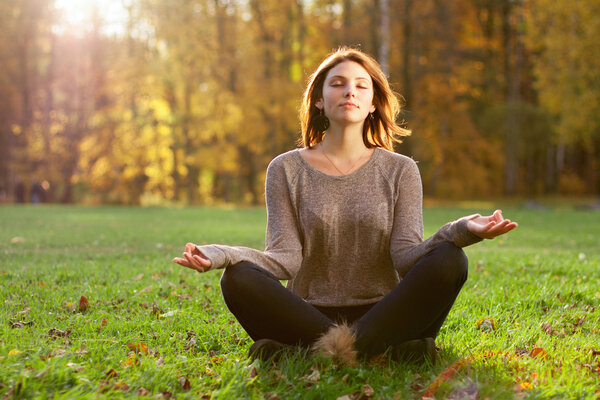 Beautiful young girl meditating in autumn park