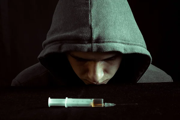 Immagine grandiosa di un tossicodipendente depresso che guarda una siringa e delle droghe — Foto Stock