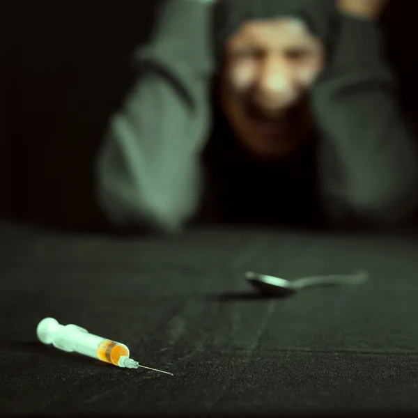 Grunge képe egy depressziós drogfüggő, látszó-on egy fecskendőt és gyógyszerek — Stock Fotó