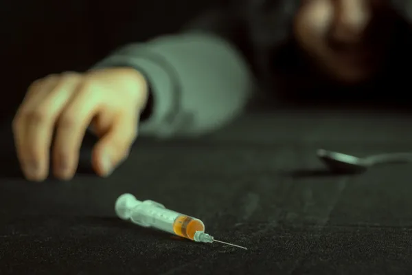 Grunge image of a depressed drug addict looking at a syringe and drugs — Stock Photo, Image