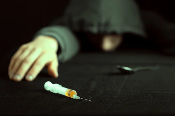 Grunge image of a depressed drug addict looking at a syringe and drugs — Stock Photo, Image