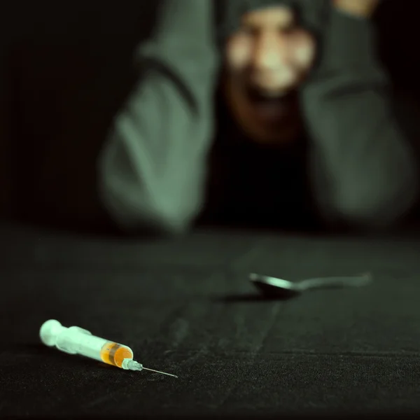 Grunge image of a depressed drug addict looking at a syringe and drugs — Stock Photo, Image