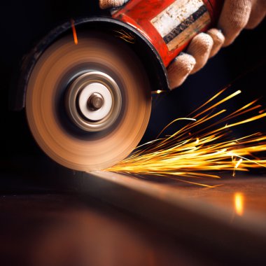 Öğütücüyle metal kesen bir işçi. Demir öğütürken kıvılcımlar