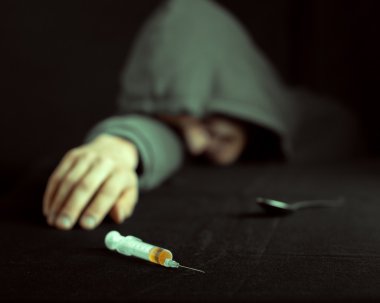 Grunge image of a depressed drug addict looking at a syringe and drugs clipart