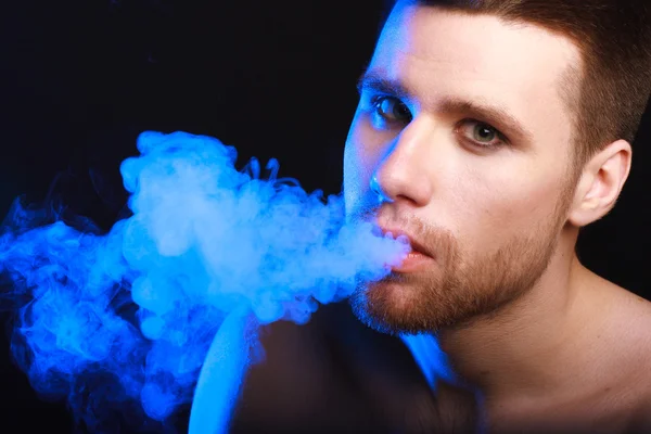 Dark and sullen shot of a young man smoking over a black background — Stock Photo, Image
