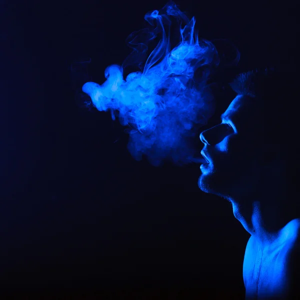 Dark and sullen shot of a young man smoking over a black background — Stock Photo, Image