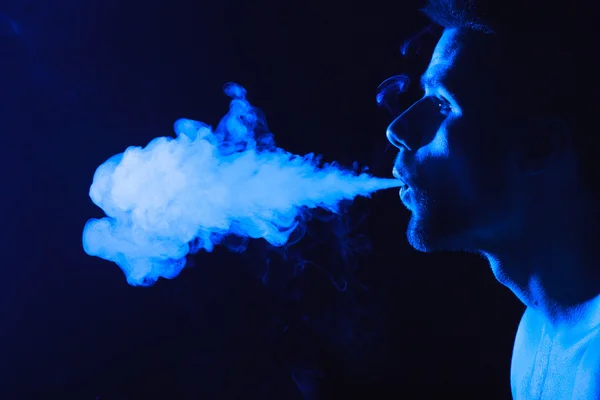 Dark and sullen shot of a young man smoking over a black background — Stock Photo, Image