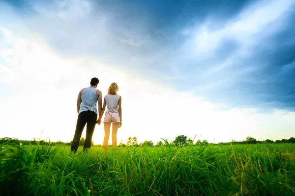 Paar geht durch das Feld und hält Händchen — Stockfoto