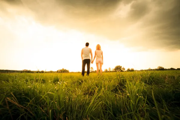 Paar geht durch das Feld und hält Händchen — Stockfoto