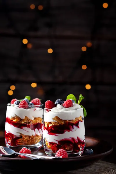 На деревянном фоне со светом, десерт со сливками, творогом, малиной и черникой в стакане — стоковое фото