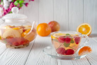 Böğürtlenli, portakallı ve beyaz ahşap arka planda cam bir çaydanlıkta naneli meyve çayı.