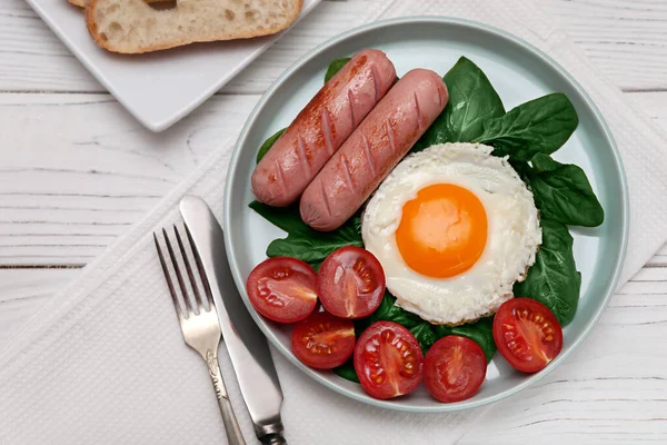 Gebakken eieren met worstjes, spinazie, tomaten, toast en sinaasappelsap op een witte houten ondergrond. Europees ontbijt. — Stockfoto