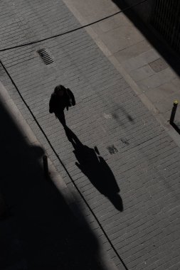 Sokakta yürüyen bir kadının en iyi görüntüsü. Yerdeki gölge. Çantası ve elinde koruyucu yüz maskesi olan bir kadın dar bir sokakta yürüyor. Yukarıdan ateş edildi..