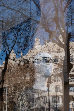 Camda güneş gözlüğü olan bir mankenin yansıması. Açık mavi gökyüzüne karşı tarihi binalar. Ön planda ağaçlar. Şehir hayatı, alışveriş, perakende, iş konsepti.