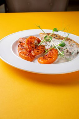 Izgara tavuk göğsü ve balkabağı izole edilmiş sarı arka planda beyaz bir tabakta.