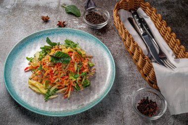 Serving a dish from the restaurant menu. Fresh salad of vegetables and beef, tomatoes, grated carrots on a blue plate against a gray stone table, a delicious appetizer