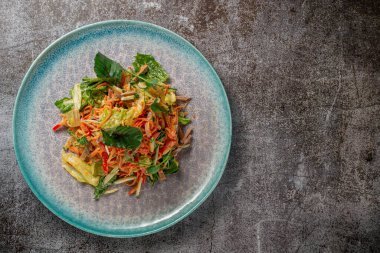 Serving a dish from the restaurant menu. Fresh salad of vegetables and beef, tomatoes, grated carrots on a blue plate against a gray stone table, a delicious appetizer