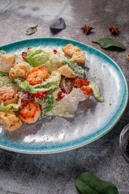 Healthy salad with fried shrimp, greens and croutons in a plate against a gray stone table. A healthy breakfast in a restaurant 