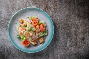 Healthy salad with greens and salmon fish in a plate against a gray stone table 