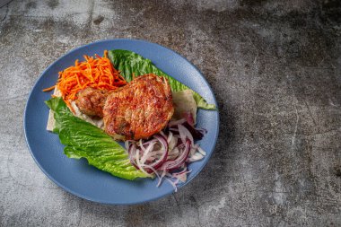 Serving a dish from the restaurant menu. Grilled beef and pork meat with grated carrots and herbs on a plate against a gray stone table, delicious kebab