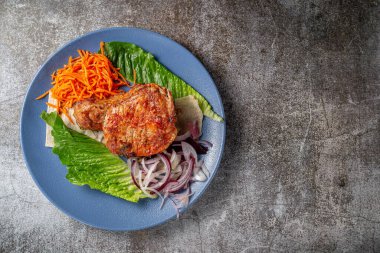 Serving a dish from the restaurant menu. Grilled beef and pork meat with grated carrots and herbs on a plate against a gray stone table, delicious kebab