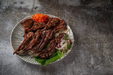 Serving a dish from the restaurant menu. Grilled beef and pork meat with grated carrots and herbs on a plate against a gray stone table, delicious kebab