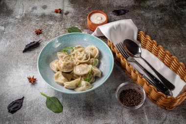 Meat dumplings with spices on a plate with greens against the background of a gray stone table 