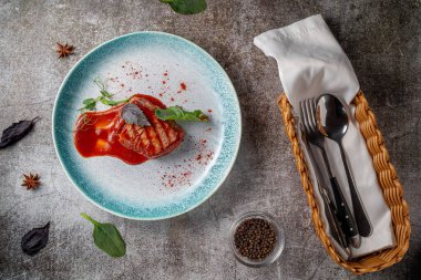 Grilled delicious beautiful meat steak in a blue plate with cutlery and a napkin on a stone table in a restaurant