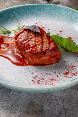 Grilled delicious beautiful meat steak in a blue plate with cutlery and a napkin on a stone table in a restaurant