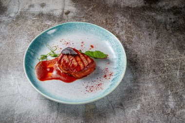 Grilled delicious beautiful meat steak in a blue plate with cutlery and a napkin on a stone table in a restaurant