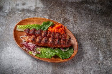 Meat kebab and barbecue with onions, Korean carrots and green salad in a plate against the background of a gray stone table 